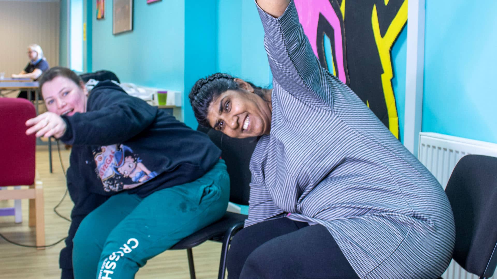 Two service users sat in chairs doing stretches with big smiles on their faces