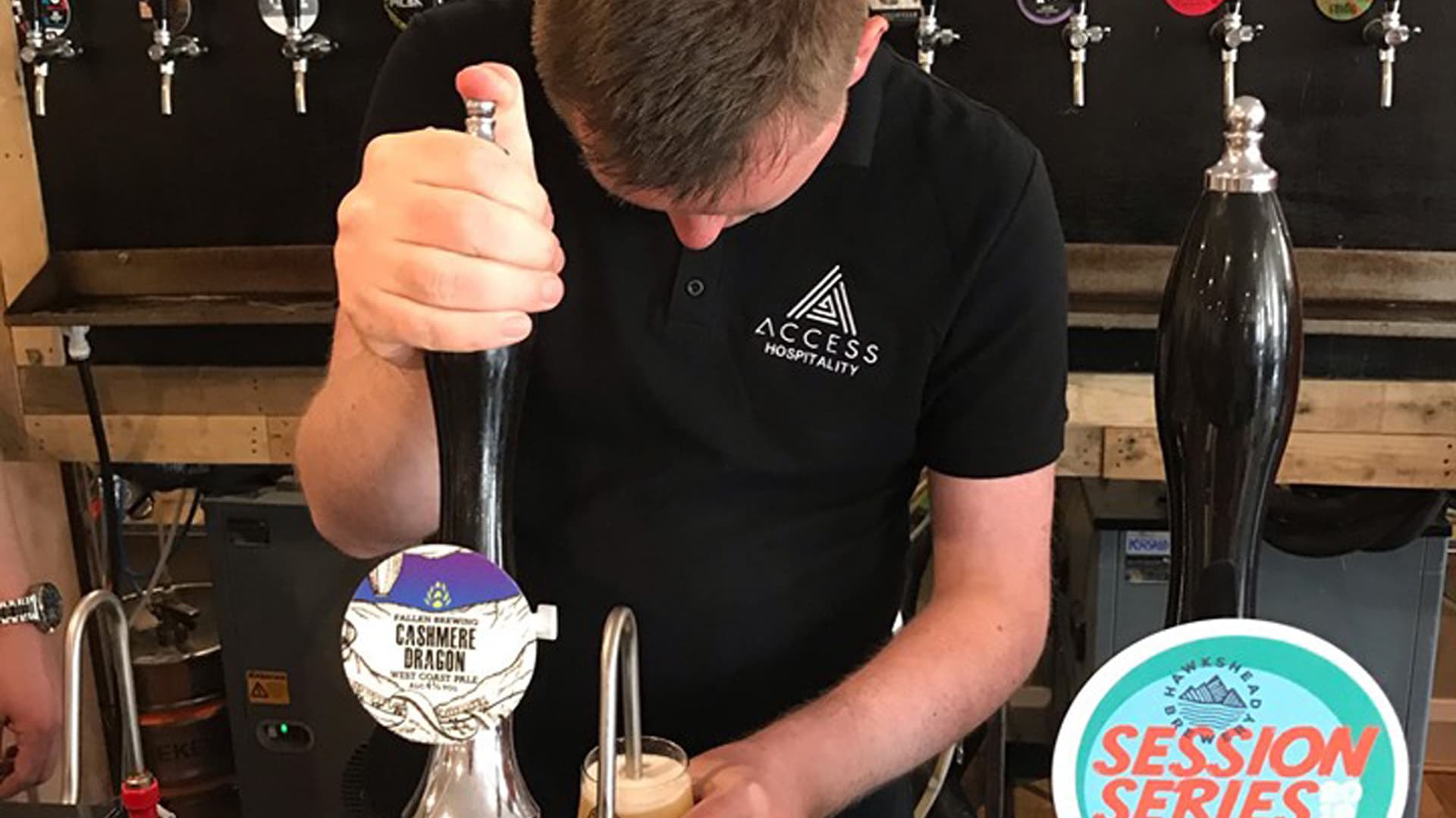 Pennine Magpies member wearing an Access Hospitality t-shirt, standing behind a bar, pulling a pint