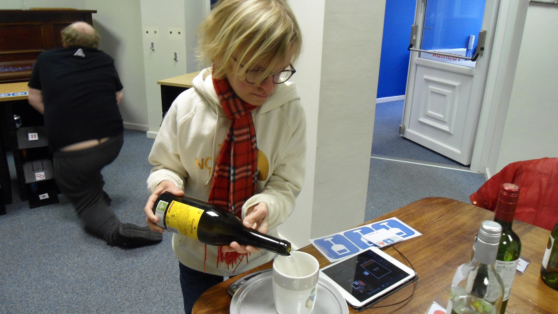 Magpies member holding a mug on a set of scales with bottles of wine, learning about drinks measurements