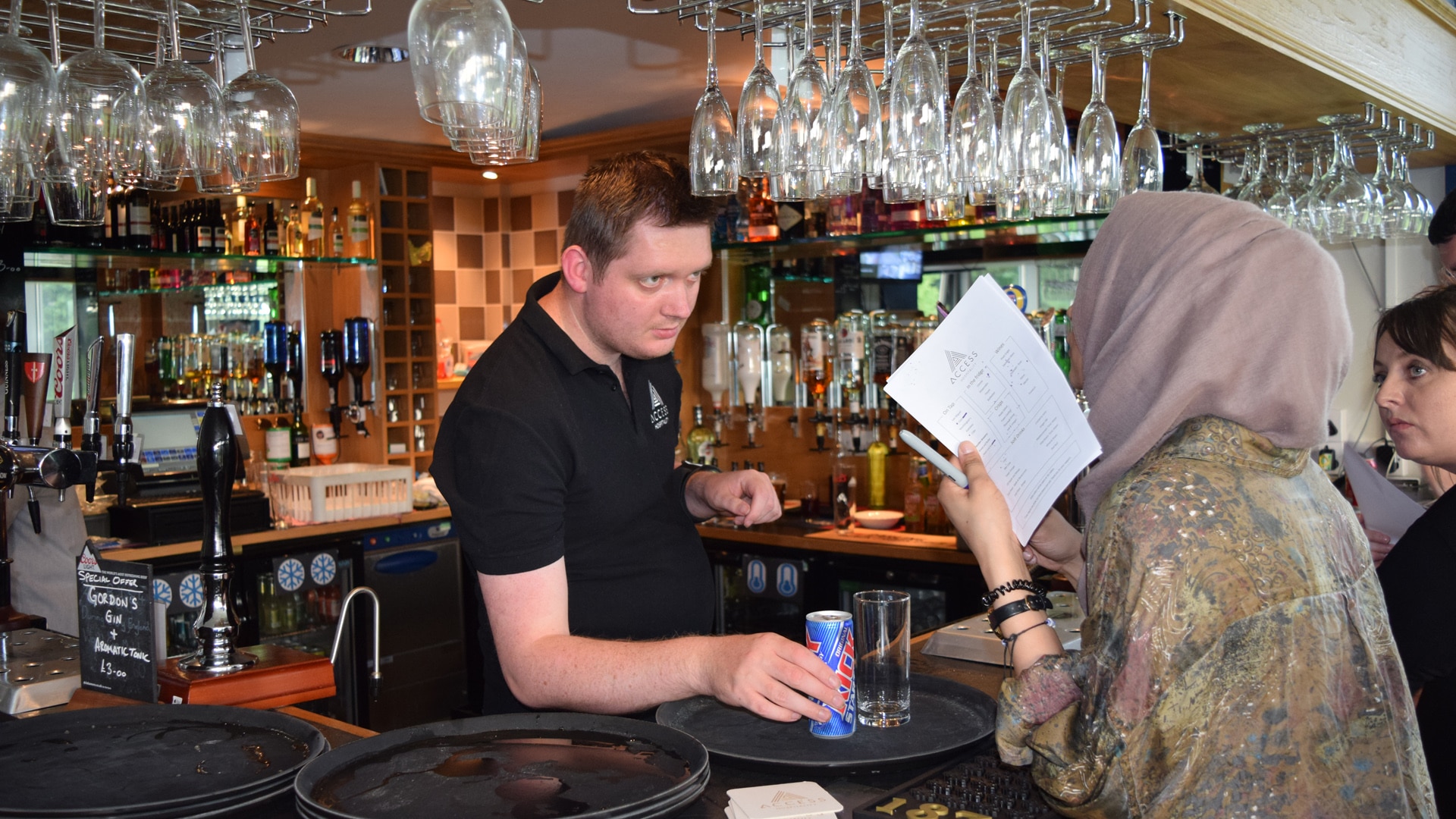 Magpies member behind a bar serving a drink to a customer